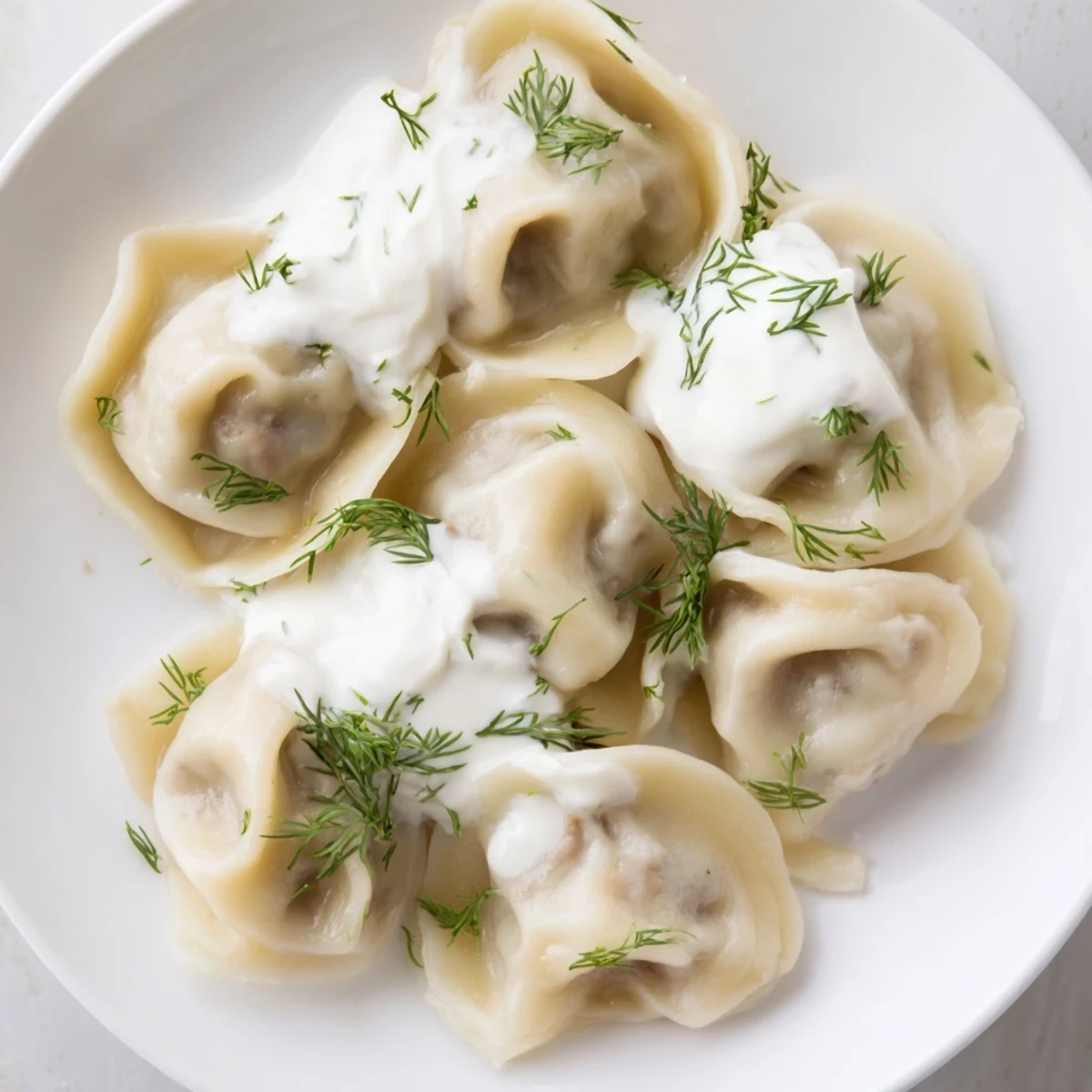 A close-up of delicious Russian pelmeni, filled with savory meat, topped with fresh dill, ready to eat.