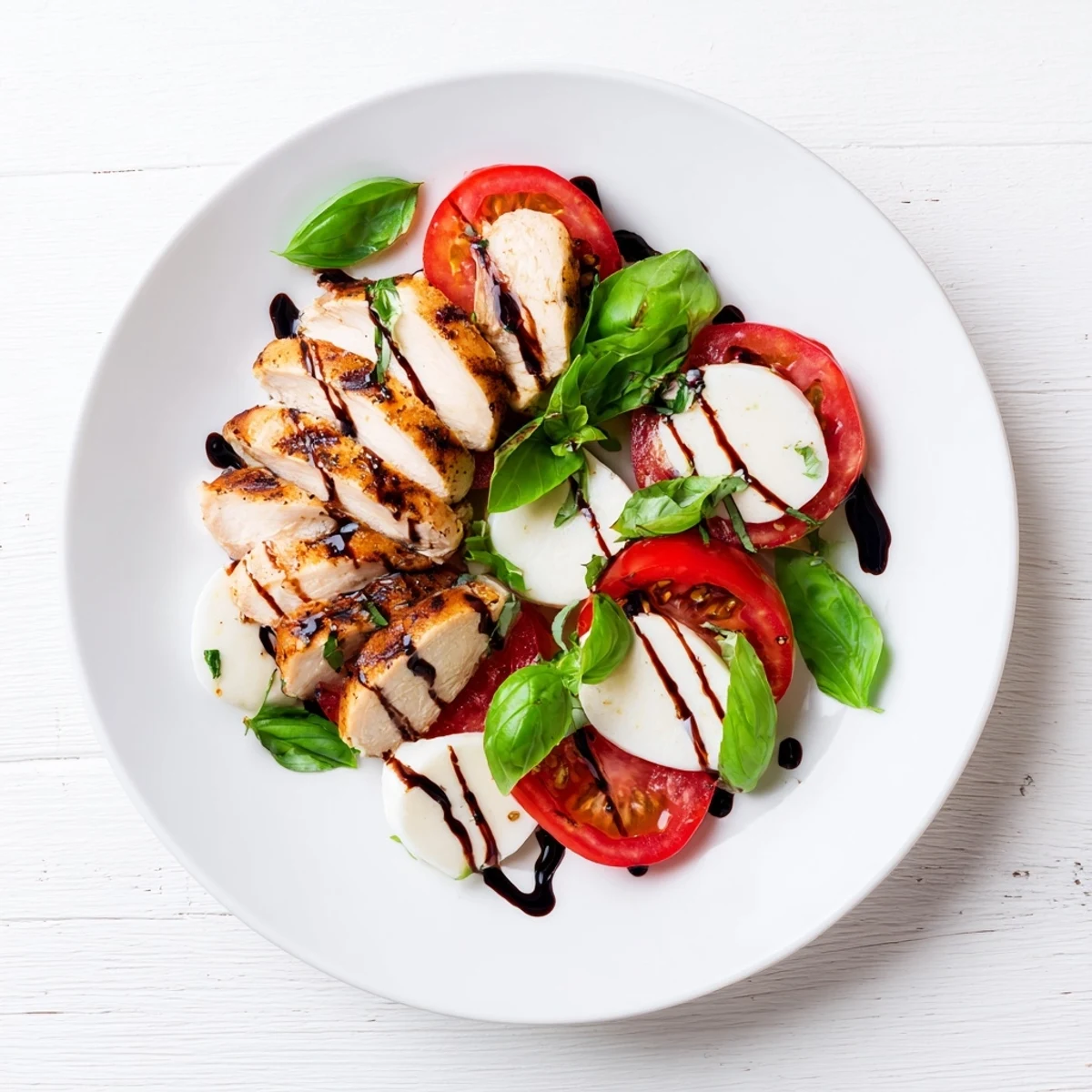 Sliced grilled chicken and creamy mozzarella on tomatoes with fresh basil, a perfect light Chicken Caprese Salad.