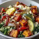 A close-up view of a vibrant warm salad bowl featuring roasted bell peppers, zucchini, and feta cheese over a bed of grains.