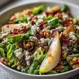A close-up of a vibrant Frisée Pear Blue Cheese Bowl topped with crispy prosciutto and toasted walnuts.
