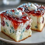Festive patriotic poke cake featuring red and blue gelatin poured into white cake, topped with creamy whipped cream and sprinkles.  
