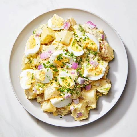 Chopped egg and potato salad, perfectly chilled, features creamy dressing and colorful vegetables, ready to eat.