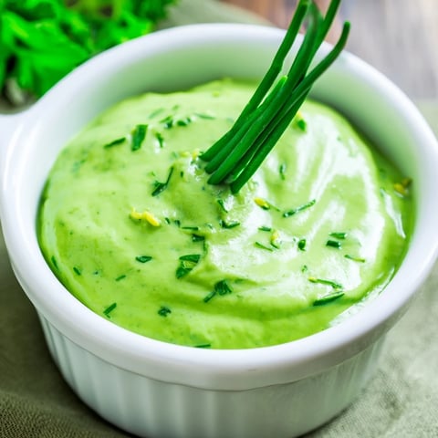 Vibrant green Goddess dressing in a glass jar, garnished with fresh herbs and lemon zest, ready for salads.  