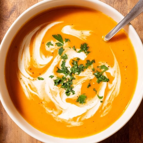 A bowl of Carrot-Based Creamy Soup with a swirl of cream, garnished with fresh parsley and served alongside crusty bread.