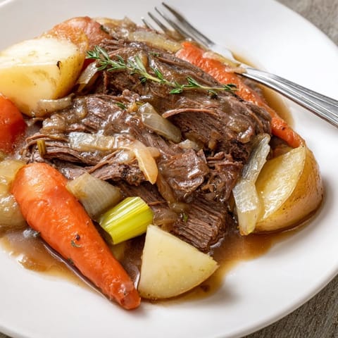 Tender beef pot roast served with hearty potatoes and aromatic herbs on a platter.  