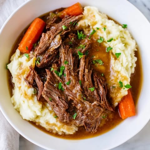 Fork-tender Slow Cooker Pot Roast, slow-cooked vegetables, and rich gravy atop creamy mashed potatoes.
