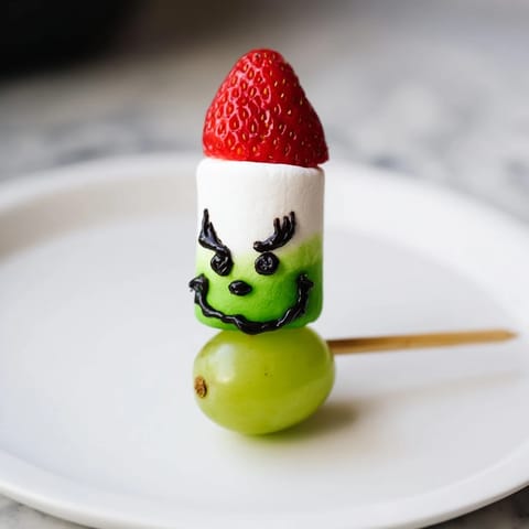 Adorable Grinch Snack with green grapes, fluffy marshmallows, and sweet strawberry santa hats.