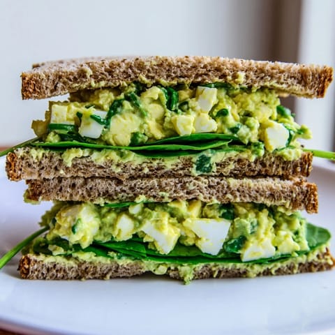 A close-up of creamy avocado egg salad sandwich with chopped eggs, lemon juice, and Dijon mustard on toasted bread.