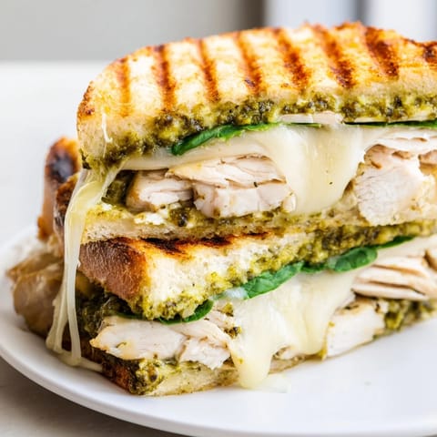 A close-up of sliced Chicken Pesto Panini revealing juicy grilled chicken layered with vibrant greens.  