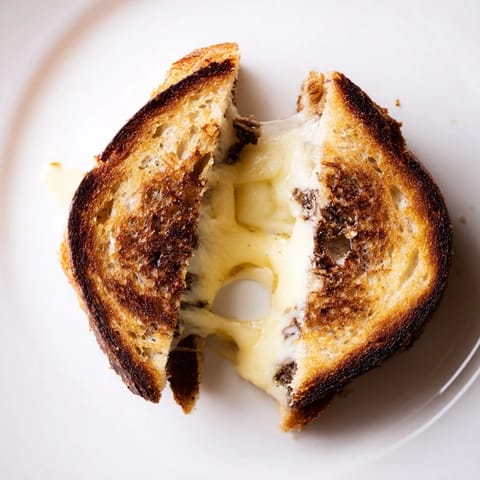 A close-up of a Truffle Grilled Cheese, revealing gooey cheese and a buttery, aromatic crust.  