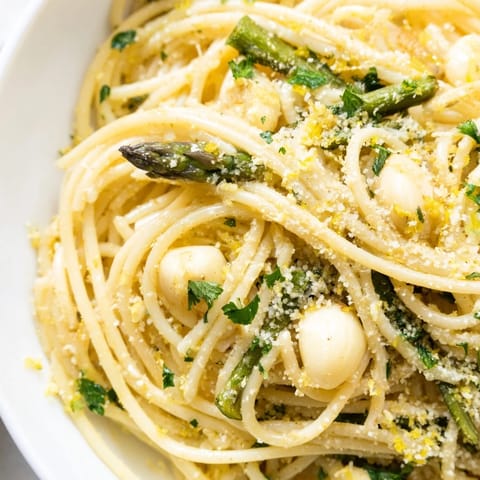 A close-up of this Roasted Garlic & Asparagus Pasta shows olive oil glistening on tender vegetables and fresh parsley garnish.