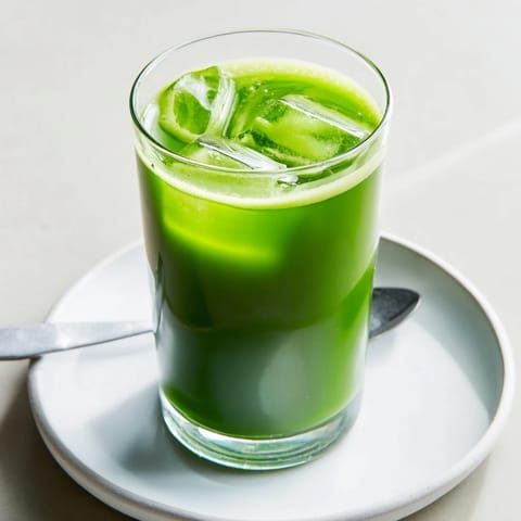 A tall glass of Cabbage and Kale Detox Juice, filled with vibrant green liquid and topped with fresh lemon and ginger slices.  