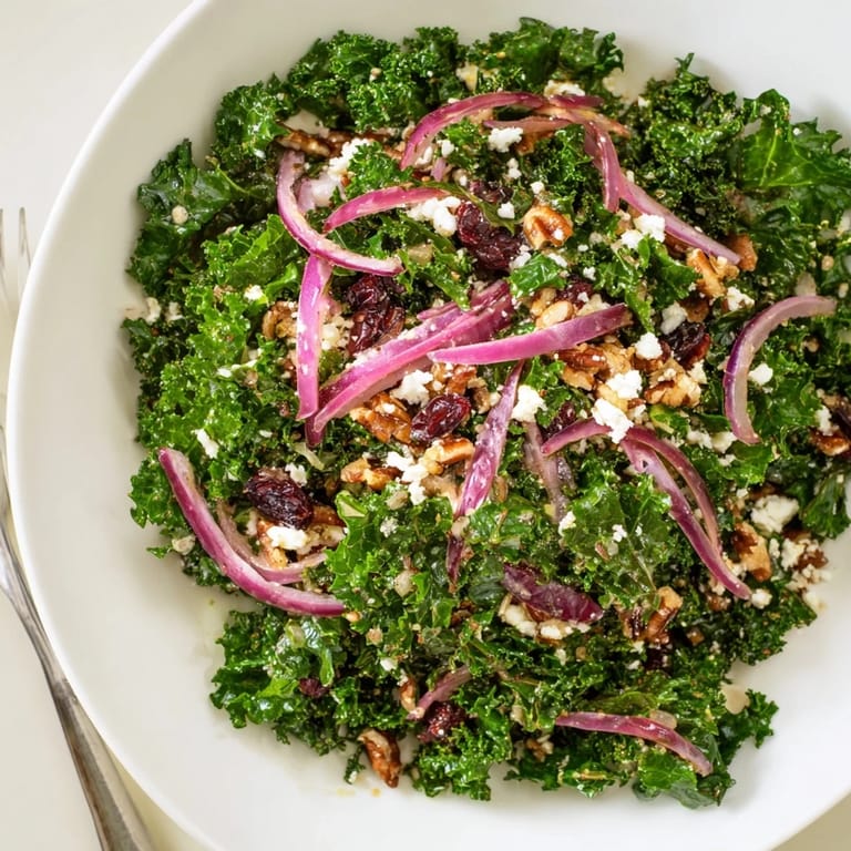A close-up view of a warm kale salad with maple mustard dressing, featuring tender kale, red onion slices, and crumbled feta cheese on a rustic platter.