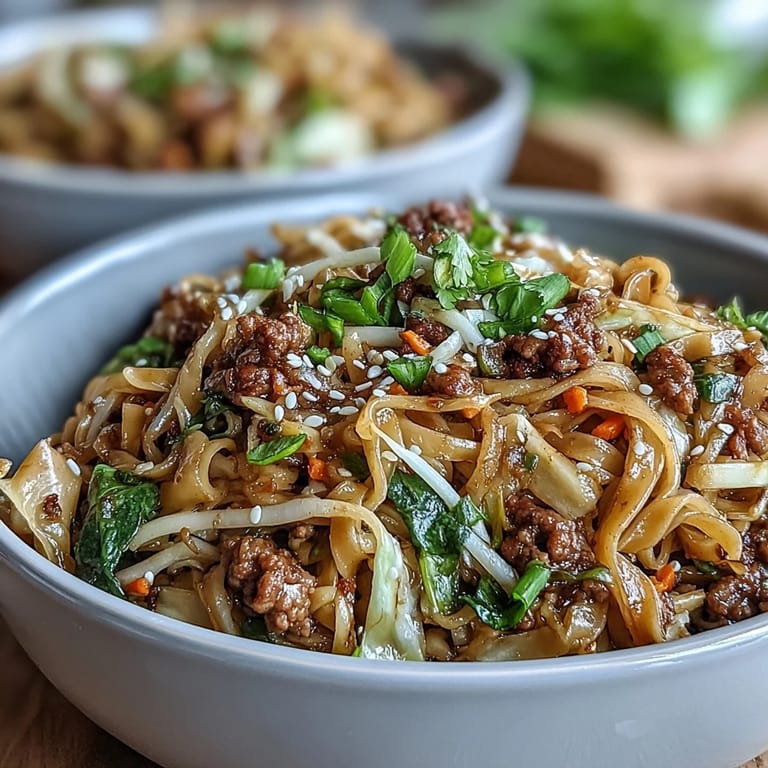 Golden brown ground pork and shredded cabbage mix with noodles in a bowl of Potsticker Noodle Bowls drizzled with chili sauce.