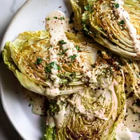 Golden-brown roasted cabbage wedges with crispy edges, drizzled with creamy tahini sauce and sprinkled with fresh parsley on a rustic platter.