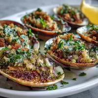 Golden-baked Roasted Clams With Lemony Panko sit on a bed of rock salt, garnished with fresh parsley and lemon wedges.