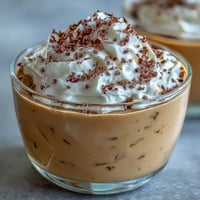 Chilled Hojicha Pudding topped with whipped cream and cocoa powder, served elegantly in a small glass.
